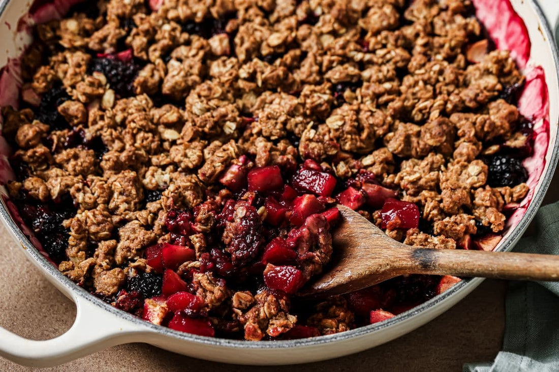 PACKD apple and blackberry crumble in a cooking bowl with a wooden serving spoon