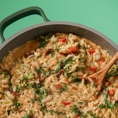 PACKD One pan creamy vegetable orzo in a pot with a wooden spoon.