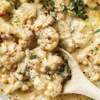 A dish of PACKD cauliflower and cheese being served with a wooden spoon