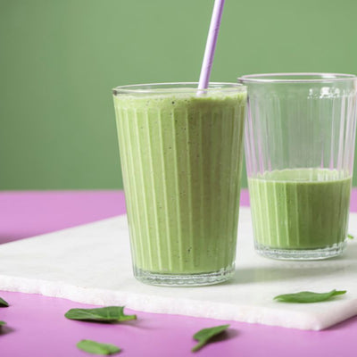 PACKD Every Day Green Smoothie in two glasses, placed on a white board on a table
