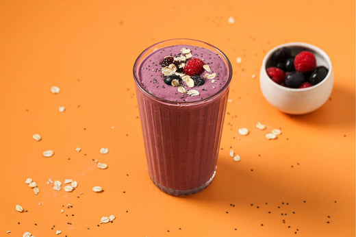 PACKD Gut health berry smoothie in a glass on a orange cloth next to a small bowl of berries