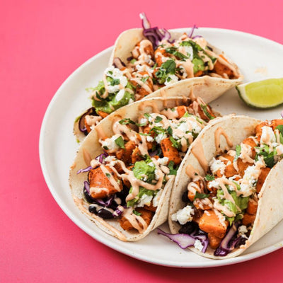 3 PACKD sweet baby tacos on a white plate with a couple of lemon slices