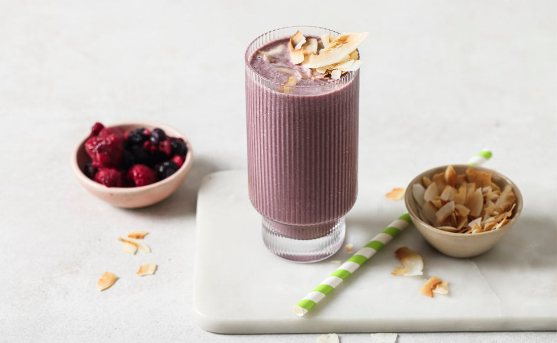 Purple berry smoothie topped with toasted coconut flakes, made with PACK'D Organic Summer Berries and frozen spinach, served with a bowl of frozen berries alongside