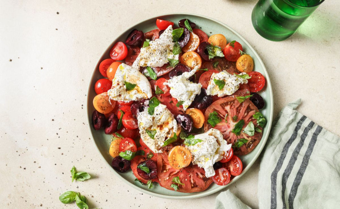 Burrata, tomato and cherry salad with torn basil, olive oil and PACK'D Organic Cherries on a green plate.