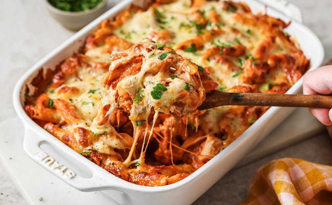 Cheesy chicken and broccoli pasta bake made with PACK'D Organic Broccoli, served from a white baking dish with melted mozzarella and parsley