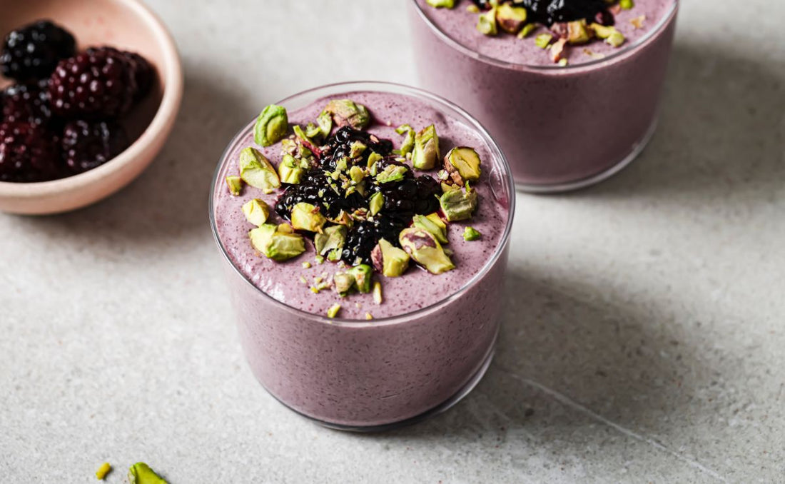 Two jars of creamy purple blended blackberry chia pudding topped with chopped green pistachios and PACK'D Organic Blackberries.