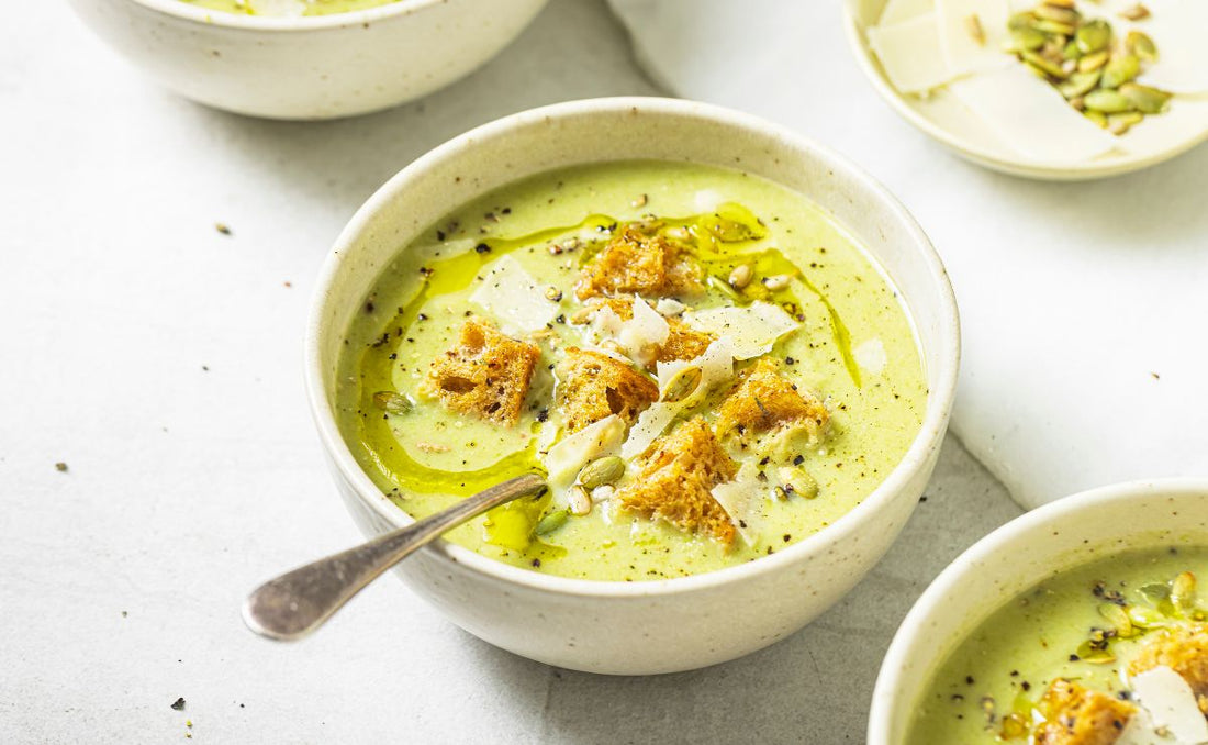 Bowl of creamy broccoli and Parmesan soup made with PACK'D Organic Broccoli, topped with croutons, Parmesan shavings, toasted pumpkin seeds, olive oil and cracked black pepper