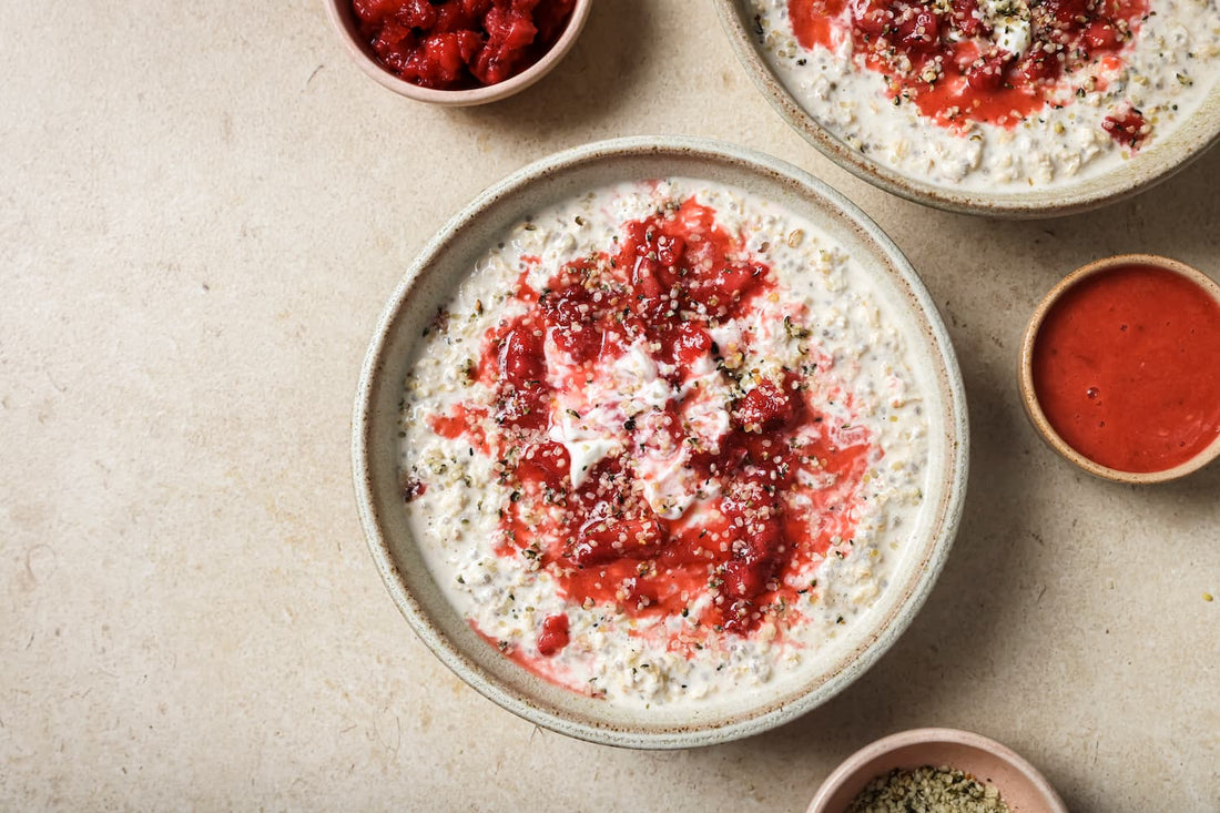 Overhead view of two bowls of creamy oats swirled with a bright red strawberry coulis and sprinkled with hemp seeds, using PACK'D organic frozen strawberries.