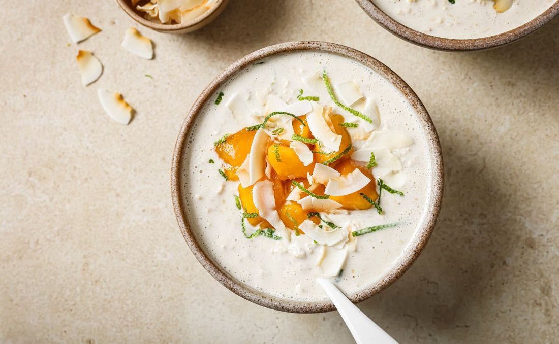 Overhead view of a ceramic bowl filled with creamy overnight oats topped with bright PACK'D organic mango chunks, toasted coconut flakes, and fresh lime zest.