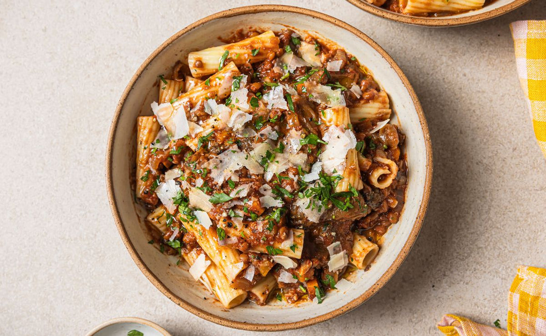 Bowl of rigatoni with roasted aubergine, mushroom and lentil ragu topped with shaved parmesan and chopped fresh herbs, made with PACK’D Organic Onions and PACK’D Organic Garlic