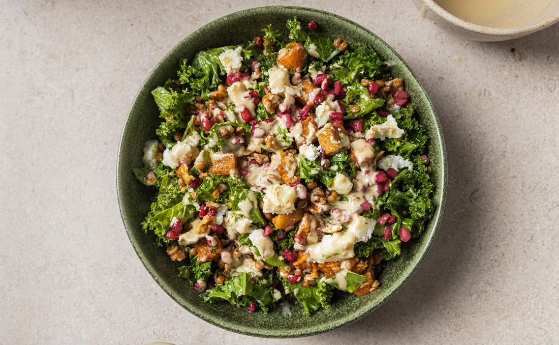 Warm sweet potato and kale salad in a green bowl with lentils, walnuts, crumbled goat's cheese, PACK'D Organic Pomegranate and a drizzle of miso tahini dressing